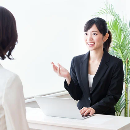 テーブル越しに来店者へ資料を示しながら説明する女性カウンセラー